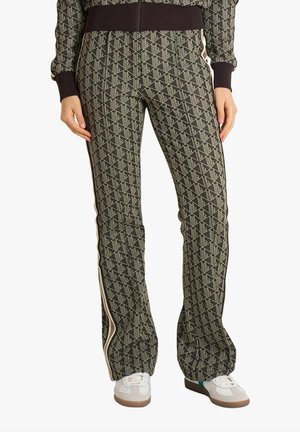 Pantaloni a sigaretta con motivo geometrico verde e nero, fascia laterale, indossati con sneaker bianche e top coordinato con lo stesso motivo.