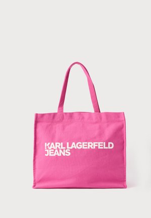 Saco de lona rosa com duas alças e texto branco grande na frente dizendo "KARL LAGERFELD JEANS". Formato retangular, textura suave.