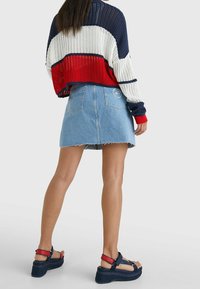 Maglione lavorato a maglia con righe rosse, bianche e blu navy, abbinato a una gonna di jeans azzurri chiari con orlo sfilacciato e due tasche posteriori. Sandali con tacco a blocco.