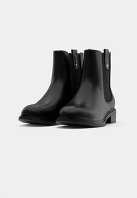 Μαύρες δερμάτινες μπότες μέχρι τον αστράγαλο με ελαστικές πλαϊνές επενδύσεις, στρογγυλή μύτη, επίπεδη σόλα και θηλιές για εύκολη εφαρμογή. Λείο υλικό και ελάχιστοι λεπτομέρειες.