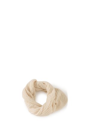 Femme portant une écharpe en tricot crème sur la tête, un pull cache-cœur crème avec une ceinture, et une jupe crème texturée sur un fond uni.