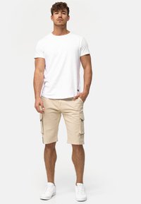 T-shirt en coton blanc associé à un short cargo beige, équipé de poches latérales, coupé juste au-dessus du genou, et des baskets blanches. Look propre et décontracté.