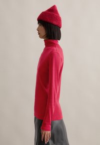 Fitted red turtleneck sweater made of soft knit fabric, paired with a black leather skirt, viewed from the side against a neutral background.