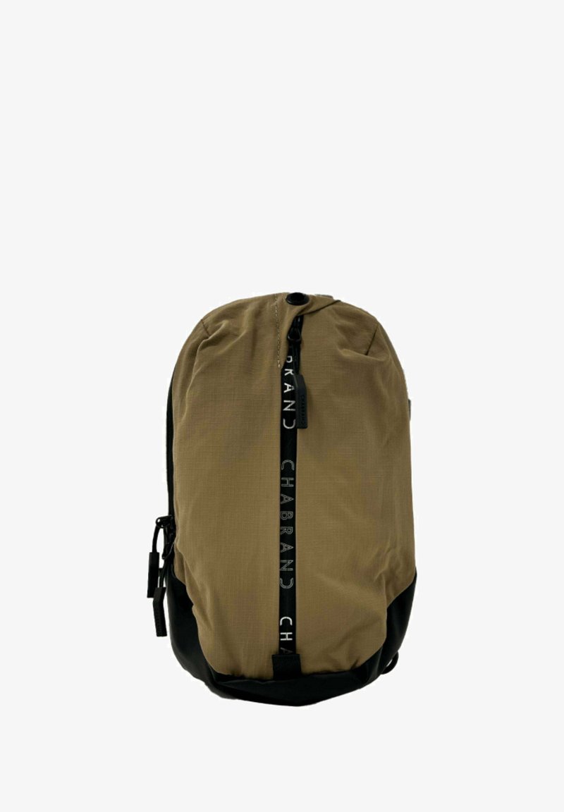 Sac à dos kaki avec fond noir, texture lisse, fermeture éclair centrale, et logo accentué sur la tirette de la fermeture et sur le panneau avant.