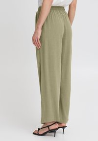 Un pantalon large vert olive clair avec une taille élastique, en tissu texturé. Associé à des escarpins noirs à lanières.