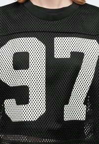 Schwarzes Mesh-Jersey mit großen weißen Zahlen "9" und "7". Strukturelle Löcher überall für Atmungsaktivität. Runder Ausschnitt und kurze Ärmel.