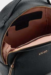 Melnas teksturētas mākslīgās ādas soma ar zelta krāsas rāvējslēdzēju un akcentiem. Iekšpusē ir gaiši rozā oderējums un zīmola etiķete.