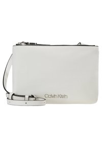 Biała skórzana kopertówka z zamknięciem na górze, regulowanym paskiem i wytłoczonym logo Calvin Klein z przodu. Gładka faktura, prostokątny kształt.