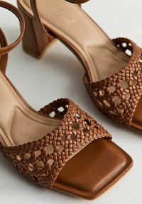 Brown woven high-heeled sandals featuring a square toe, open upper design, and a smooth leather-like ankle strap.