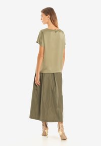 Blusa verde oliva a maniche corte realizzata in tessuto liscio, abbinata a una gonna maxi plissettata in un materiale più morbido.
