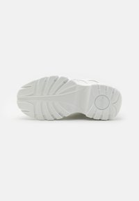 Semelle de chaussure de sport blanche, dotée d'une surface en caoutchouc texture avec des rainures multidirectionnelles et un logo circulaire au niveau du talon.