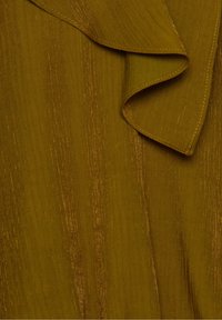 Gros plan sur un tissu jaune moutarde avec un léger éclat vertical et un détail à bordure froncée.