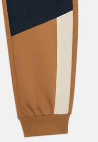 Farbblockierte Jogginghosen in Braun, Marineblau und Creme. Hergestellt aus weichem Strickstoff, mit elastischen Bündchen und ausgeprägten geometrischen Mustern.