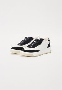 Sneakers with a white leather upper, black suede accents, and a textured cream rubber sole. Features black laces and padded ankle support.