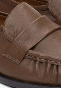 Brown leather moccasin shoe featuring a large bow accent, textured upper, gathered detailing along the edge, and dark sole.