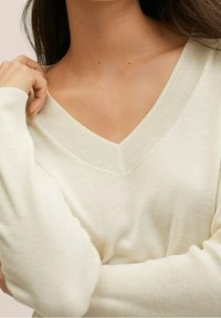 Pull crème en V à manches longues, avec une texture côtelée et une coupe ajustée. Le tissu lisse tombe doucement sur la peau.