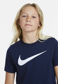 Tmavě modré tričko Nike z bavlněné směsi s velkým bílým logem na hrudi; krátké rukávy, kulatý výstřih, hladká textura.