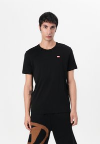 Sort kortærmet t-shirt lavet af bomuld, med rund halsudskæring og et lille rødt logo på den øverste venstre bryst. Enkel design.