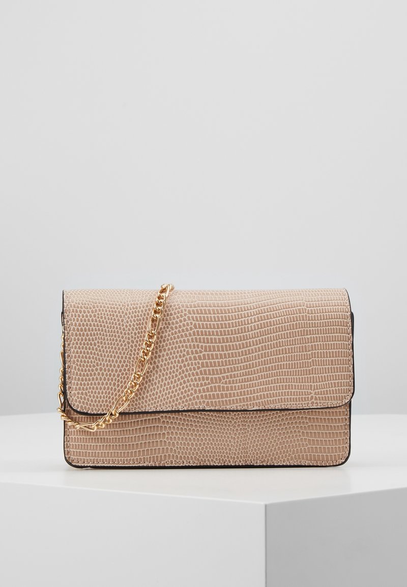 Beige texturovaná kabelka s klopou a zlatým řetízkem, vystavená na bílé podstavě proti neutrálnímu pozadí.