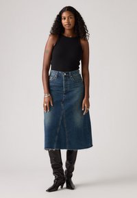 Denim maksi suknja tamnoplave boje s prednjim prorezom, nosi se s crnim topom bez rukava i crnim čizama do koljena. Ima strganu donju ivicu i pet džepova.