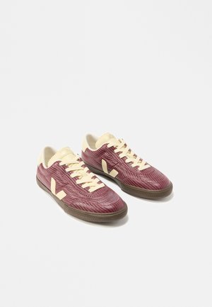 Pair of low-top sneakers in maroon textured fabric with cream laces, heel, and logo, and dark rubber soles shown on white background.