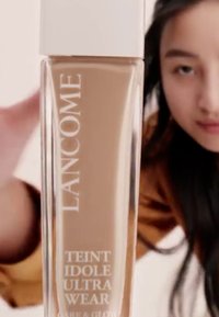 Lancôme Teint Idole Ultra Wear-foundation i en klar glassflaske med et hvitt lokk, som viser en beige farge merket for enkel identifikasjon.