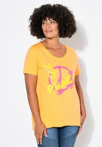 T-shirt jaune à manches courtes avec un décolleté en scoop présentant un symbole de paix rose et un graphique "PAIX" en texte jaune en gras. Matériau doux.