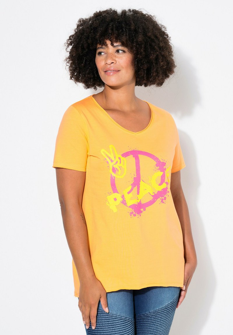 T-shirt jaune à manches courtes avec un décolleté en scoop présentant un symbole de paix rose et un graphique "PAIX" en texte jaune en gras. Matériau doux.