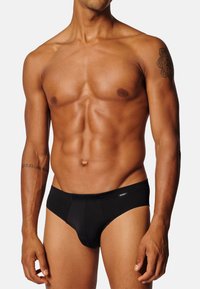 Slip nero realizzato in tessuto liscio, con un design aderente e un elastico in vita. Il tessuto appare morbido ed elastico.