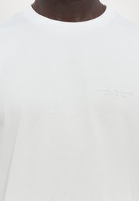Hvit bomull t-skjorte med rund hals, som har en subtil preget logo med teksten "Armani Exchange Milano/New York" på brystet.