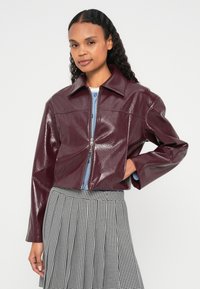 Vijolično lakasto skrajšano jakno z ostrim ovratnikom in zadrgo. Model nosi svetlomodro majico in črno-belo krilo v vzorcu psje zob.