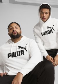 Hanorace albe dintr-un material neted, cu un mare logo negru "PUMA" și silueta unei feline. Designul include șnururi și buzunare tip kangur.