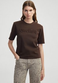 Bruine katoenen t-shirt met een ronde hals, korte mouwen, met een textuur "tessallate" borduursel en versieringen aan de voorkant.