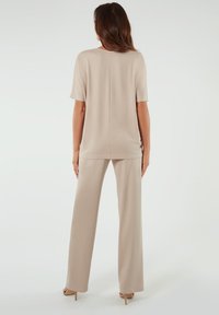Beżowy sweter z krótkimi rękawami i luźnym krojem, zestawiony z pasującymi beżowymi spodniami o szerokich nogawkach. Gładka tekstura, prosty design i brak wzorów.