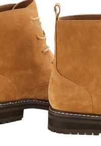 Bottines en daim tan avec des orteils ronds, des accents cousus et une semelle en caoutchouc texturé. Dotées d'un système de laçage et d'une languette au talon.