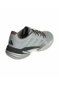 Scarpa sportiva grigia con una parte superiore testurizzata, accenti marroni, dettagli in argento e un design della suola curvato. Presenta tre strisce sul lato.