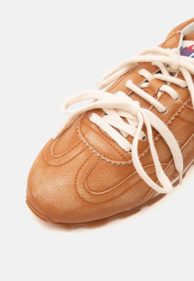 Baskets en cuir marron avec des lacets blancs noués en nœud, montrant des coutures détaillées et une surface texturée sur fond blanc.