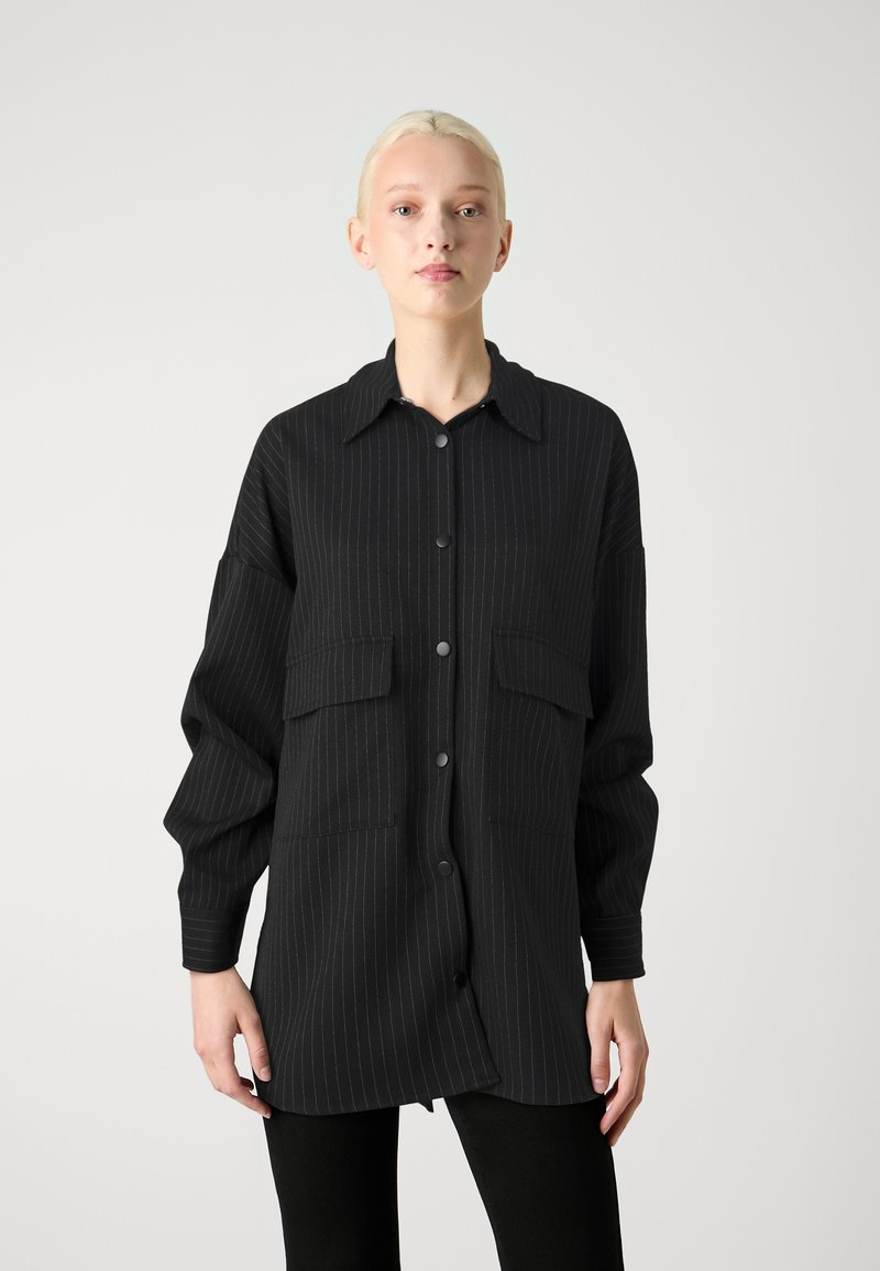 Giacca camicia nera a righe con maniche lunghe, chiusura con bottoni, due tasche sul petto e colletto a punta in tessuto leggero.
