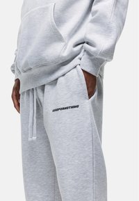 Grijze katoenen sweatshirt met een voorzak, gecombineerd met grijze joggingbroek met een zwart "GOODFORNOTHING" logo op de dij.