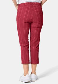Rot gestreifte Caprihosen mit einem elastischen Bund, ausgestattet mit einer glatten Stoffoberfläche und verkürzter Länge, kombiniert mit weißen Sneakers.