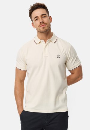 Bež polo majica s ovratnikom, s bordo detaljima. Kratki rukavi i mali logotip na lijevoj strani prsiju. Glatka tekstura tkanine.