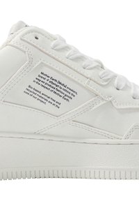 Hvit sneaker med glatt skinnopplegg, avrundet tå og teksturert gummisåle. Har en sydd etikett med tekst om miljøvennlighet.