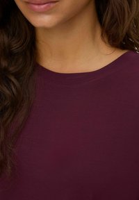 Bordeauxskjorta med rund halsringning, tillverkad av mjukt bomullsmaterial. Slät textur och korta ärmar, med minimala sömnadsdetaljer.