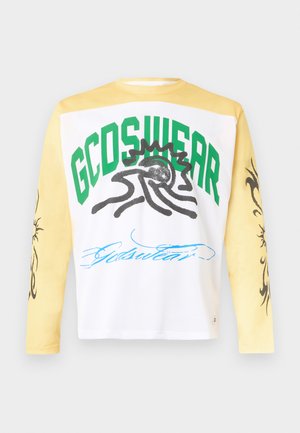Μπλούζα με μακριά μανίκια και κίτρινα μανίκια· το λευκό πάνελ στο στήθος έχει πράσινο κείμενο "GCDS WEAR", μαύρο αφηρημένο γραφικό ήλιου και μπλε γραφή από κάτω.