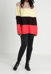 Pull tricot multicolore avec des rayures horizontales en beige, jaune, brun foncé et corail. Coupe ample, encolure ronde et ourlet côtelé.