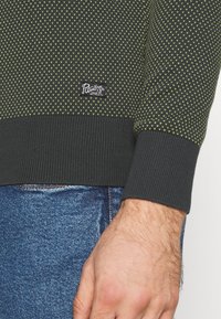 Neulottu tumma vihreä villapaita, jossa pieniä keltaisia kolmionmuotoisia kuvioita. Resorit hihansuissa ja helmassa. Sivussa ommeltu brändäyslappu.