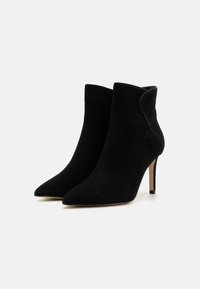 Bottines en daim noir avec un bout pointu et un talon aiguille haut. Présentent un design courbé au niveau de la cheville pour plus de détails.