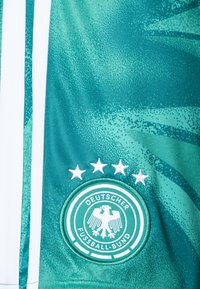 Zelený športový dres s textúrovaným vzorom, bielymi akcentmi a okrúhlym vyšívaným odznakom s dvojhlavým orlom a štyrmi hviezdami.