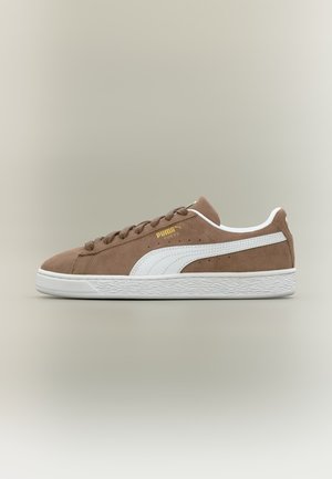 Hnedá semišová teniska Puma s bielou podrážkou a pruhom, zlaté logo Puma, bočný pohľad na neutrálnom pozadí.