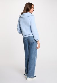 Chaqueta de forro polar azul claro con un amplio cuello, diseño corto y dobladillo acanalado; combinada con unos vaqueros azules de cintura alta y corte holgado.